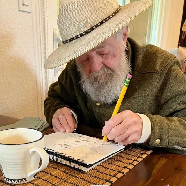 Uncle Jack, in a hat, writes in a notebook at a table with a coffee mug.